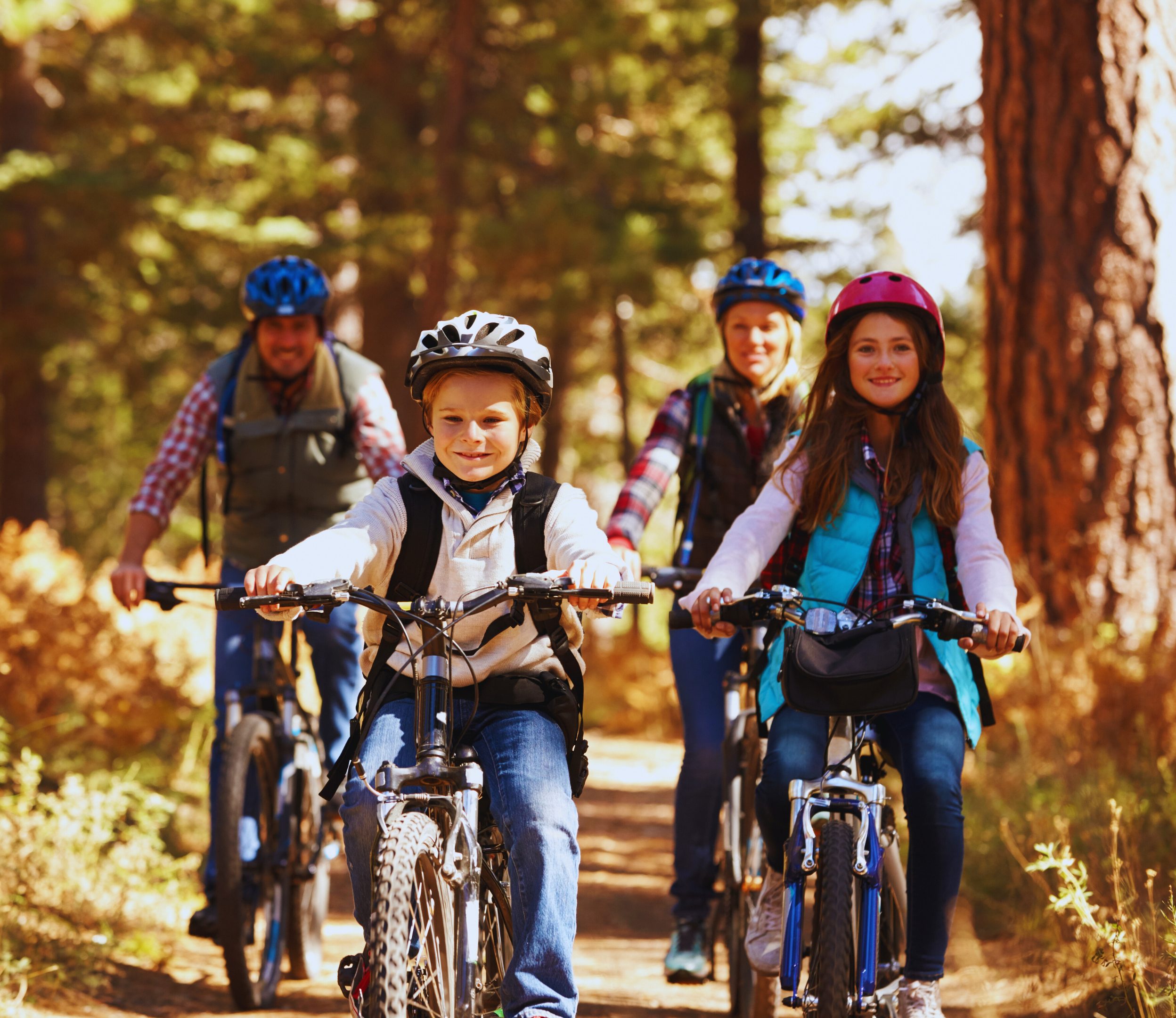 FamilyCycling_HealthWellnessCause_Header Parents and children riding bikes on a forest trail.