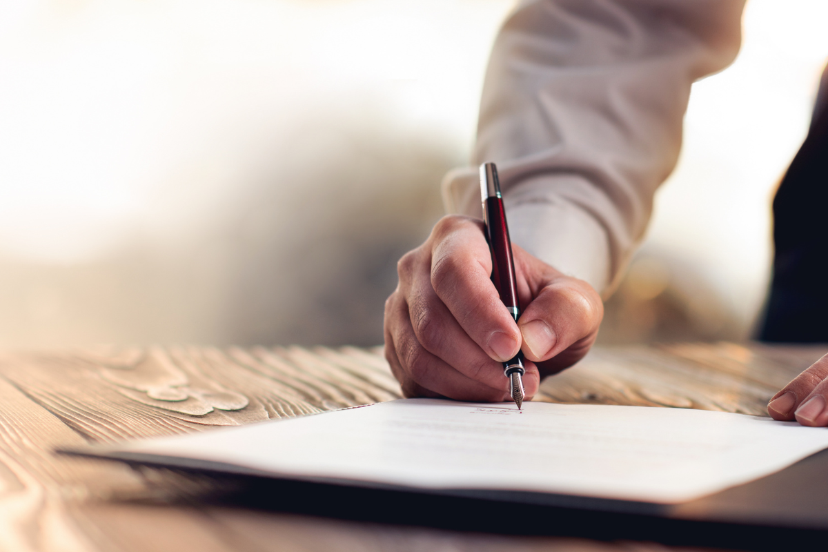 Someone's hand filling out a paper will with a pen.