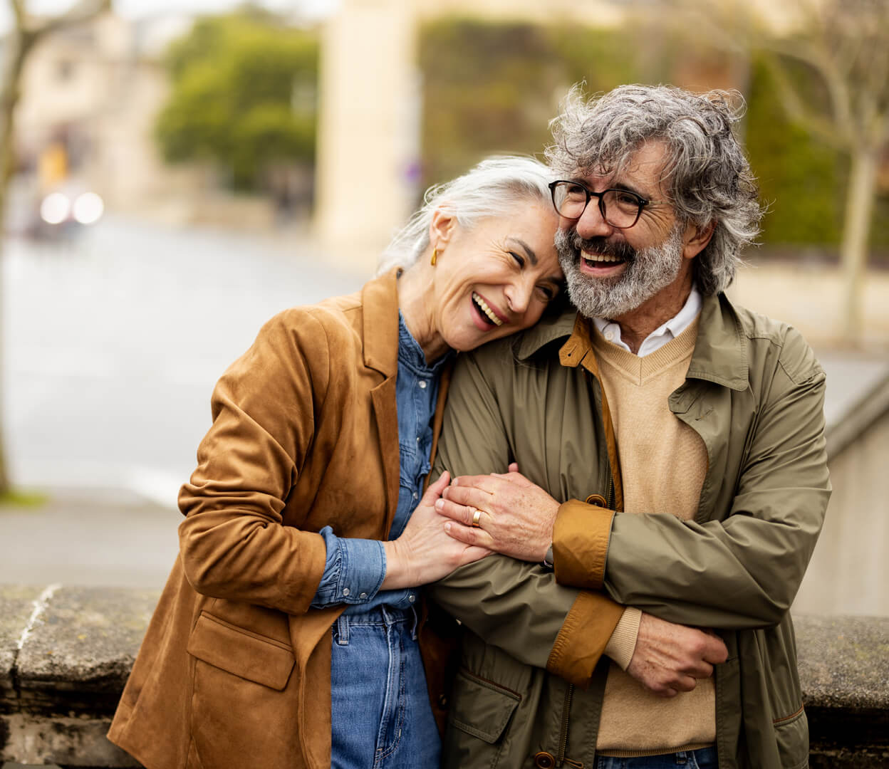 A couple embrace and laugh as they walk down an outdoor street.