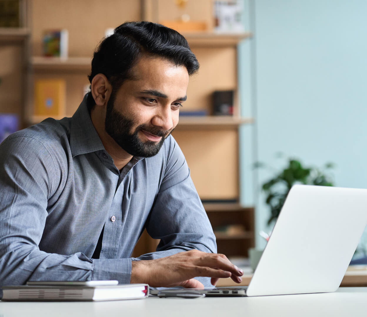 A man smiles while navigating a website on his laptop.
