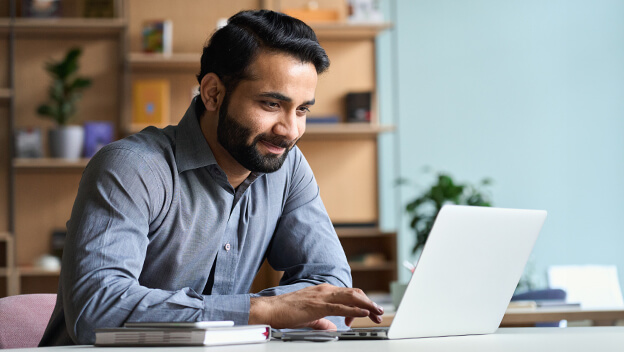 A man smiles while navigating a website on his laptop.