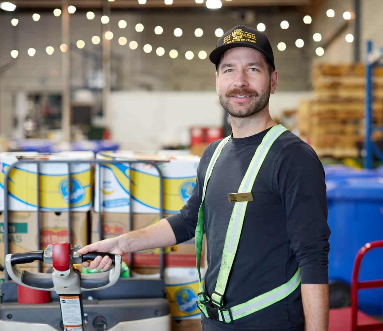 A man looks proudly at the camera while moving a palette full of rescued food at the Mustard Seed Food Security Distribution Centre.