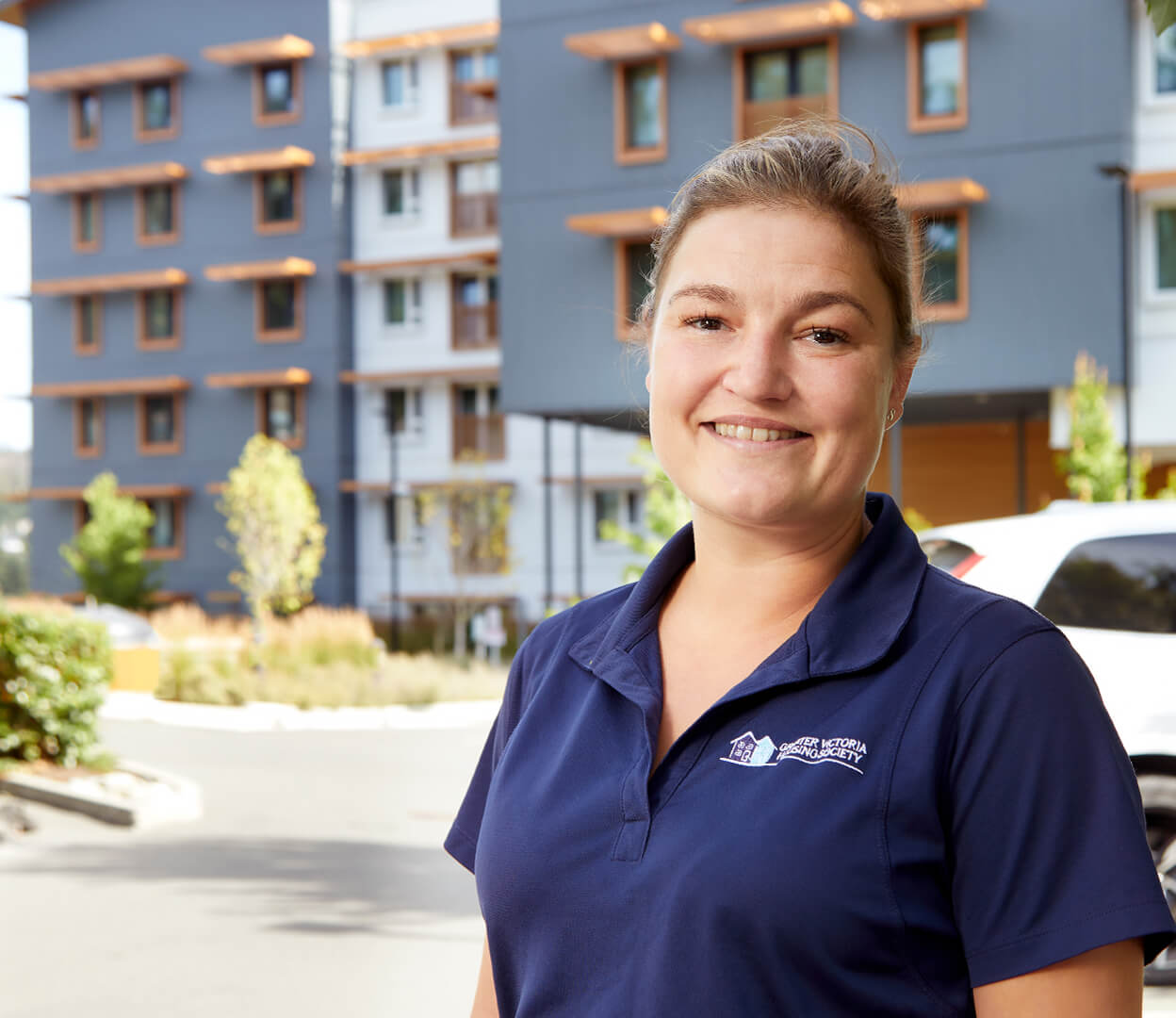 A woman from the Greater Victoria Housing Society stands proudly in front of a newly constructed housing project.