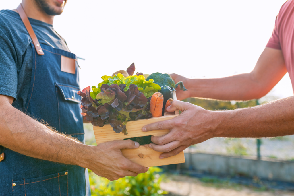 Someone handing another person a box of garden produce.