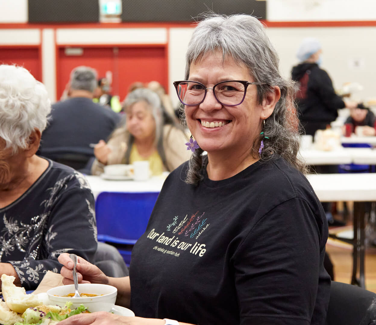 A woman smiles at the camera while enjoying lunch at the Victoria Native Friendship Centre.