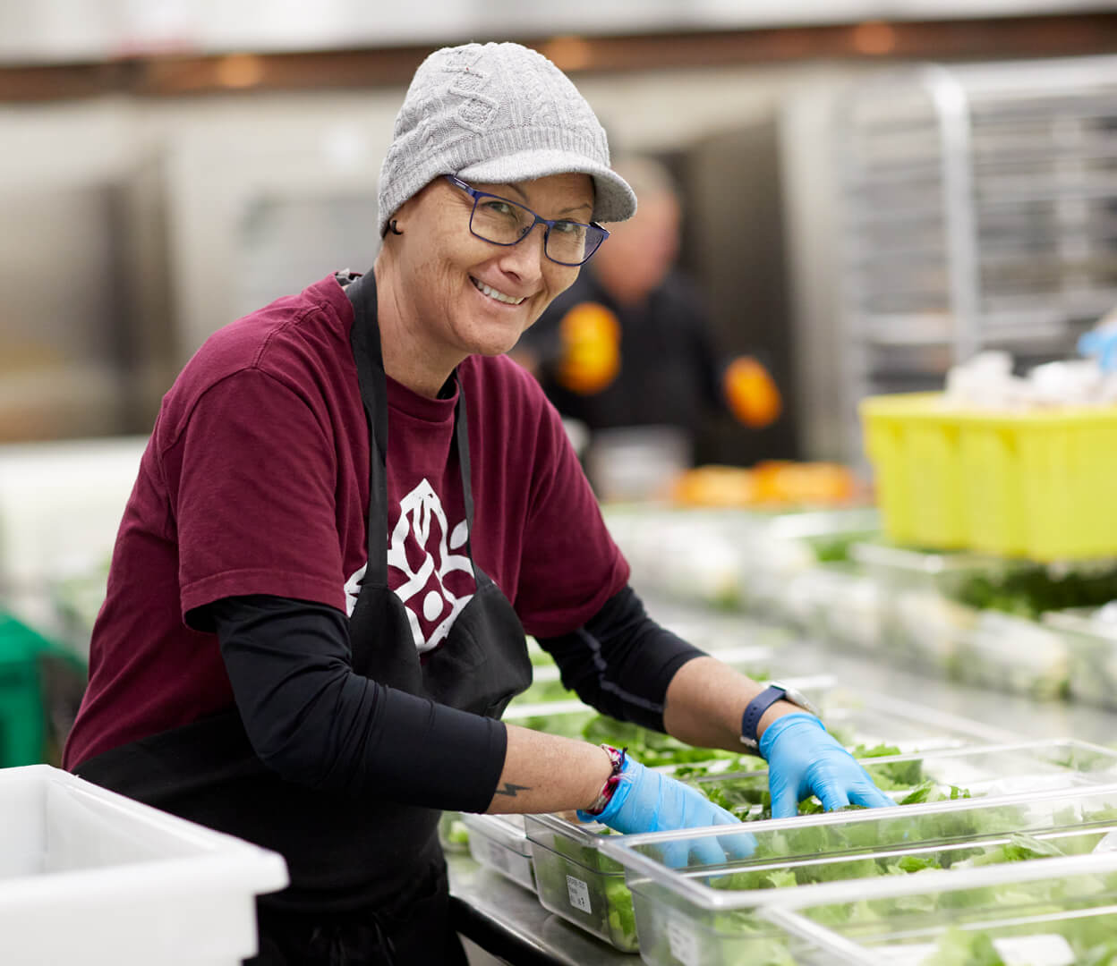 A woman smiles at the camera while assembling food baskets at the Mustard Seed Food Security Distribution Centre.