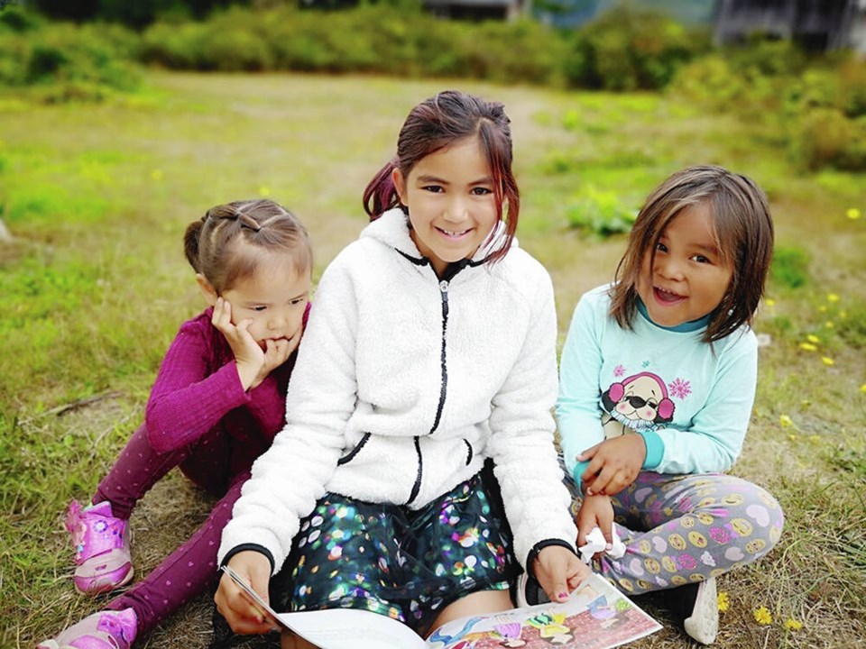 Young children sit in a field reading a book.