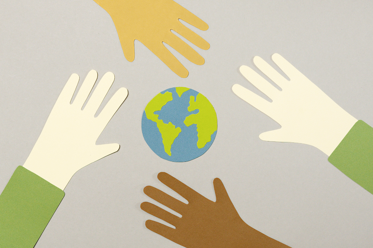 Hands of different colours reach out toward a small globe.
