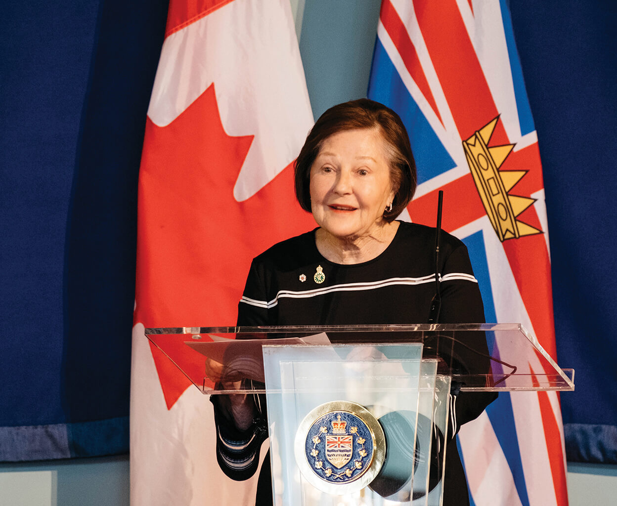 Sandra Richardson speaking at a lecturn in front of the British Columbia flag